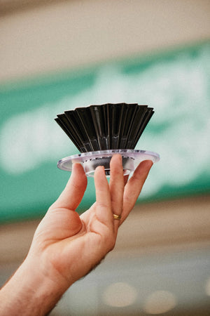 Hand holding up a Origami Brewer, infront of the Audrey Coffee sign.