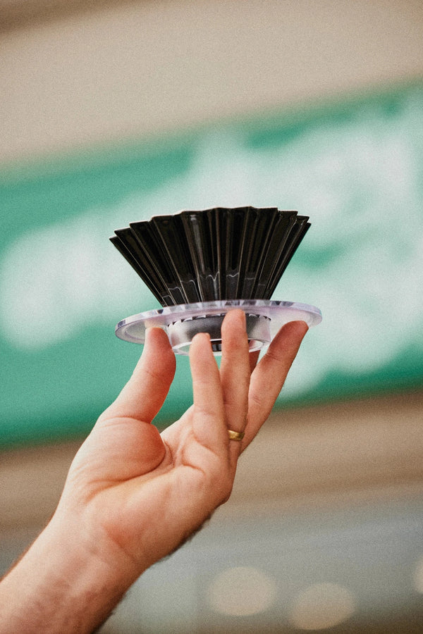 Hand holding up a Origami Brewer, infront of the Audrey Coffee sign.