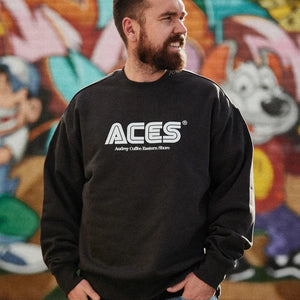 Man with hands in jean pockets, looking away from camera, wearing a black jumper with ACES Audrey Coffee Eastern Shore written on it