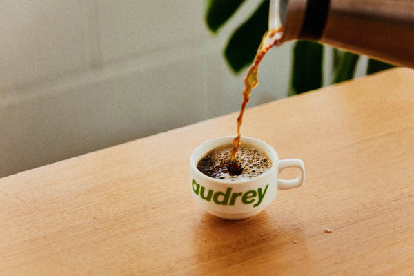 Coffee being messily poured into an audrey coffee branded cup, on a wooden table at their second Hobart coffee shop
