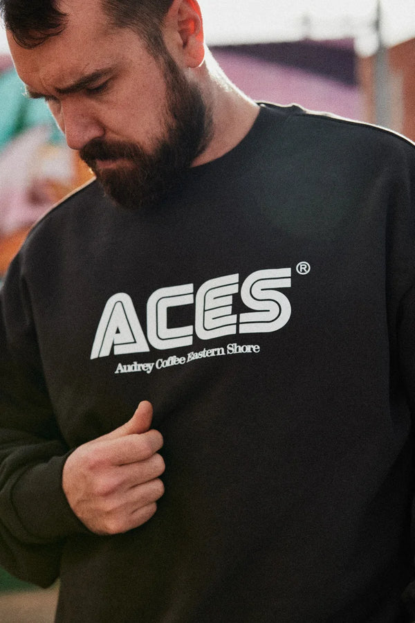 Man, looking away from camera, wearing a black jumper with ACES Audrey Coffee Eastern Shore written on it